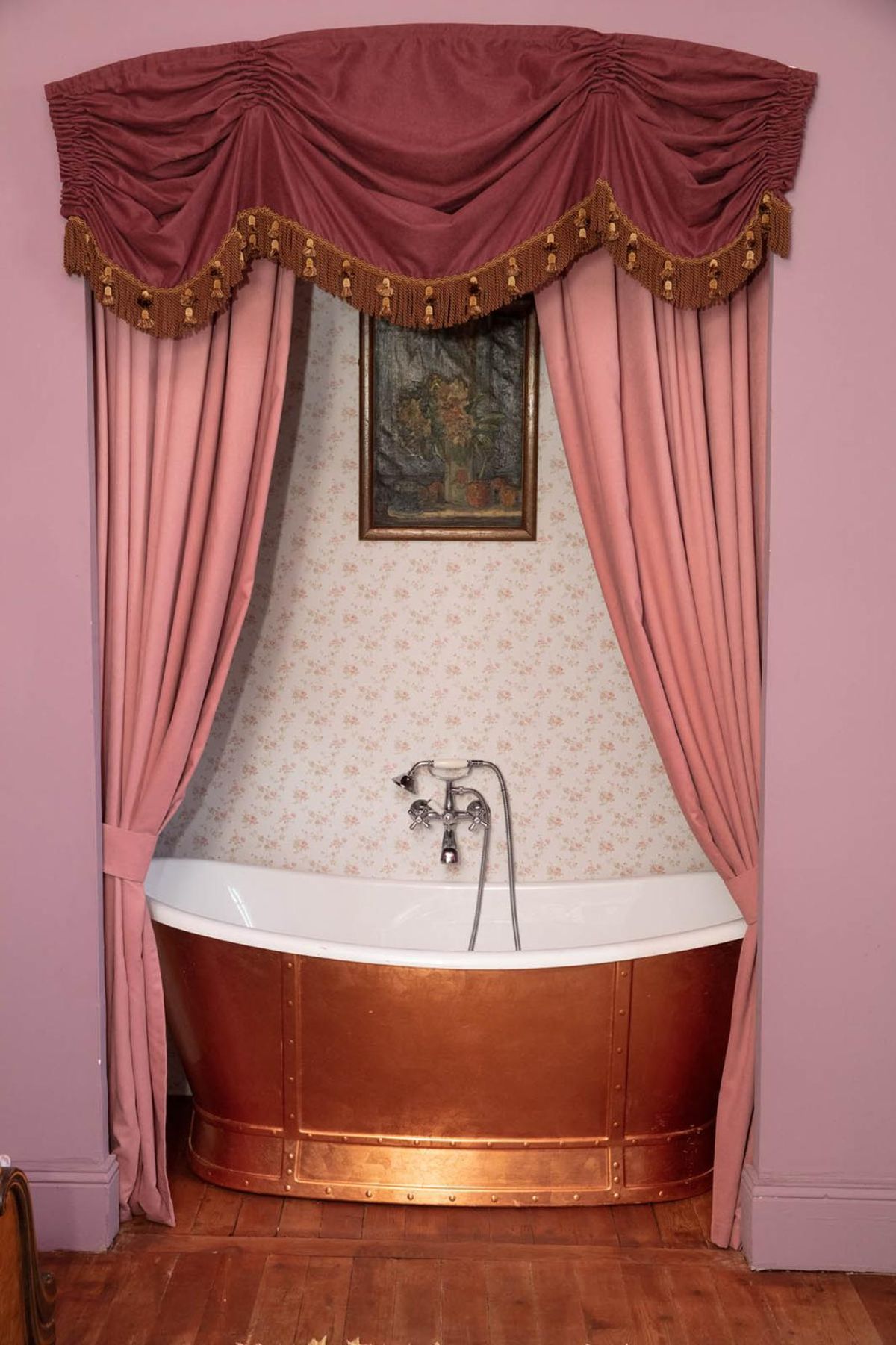 A copper bathtub in a curtained alcove with pink walls