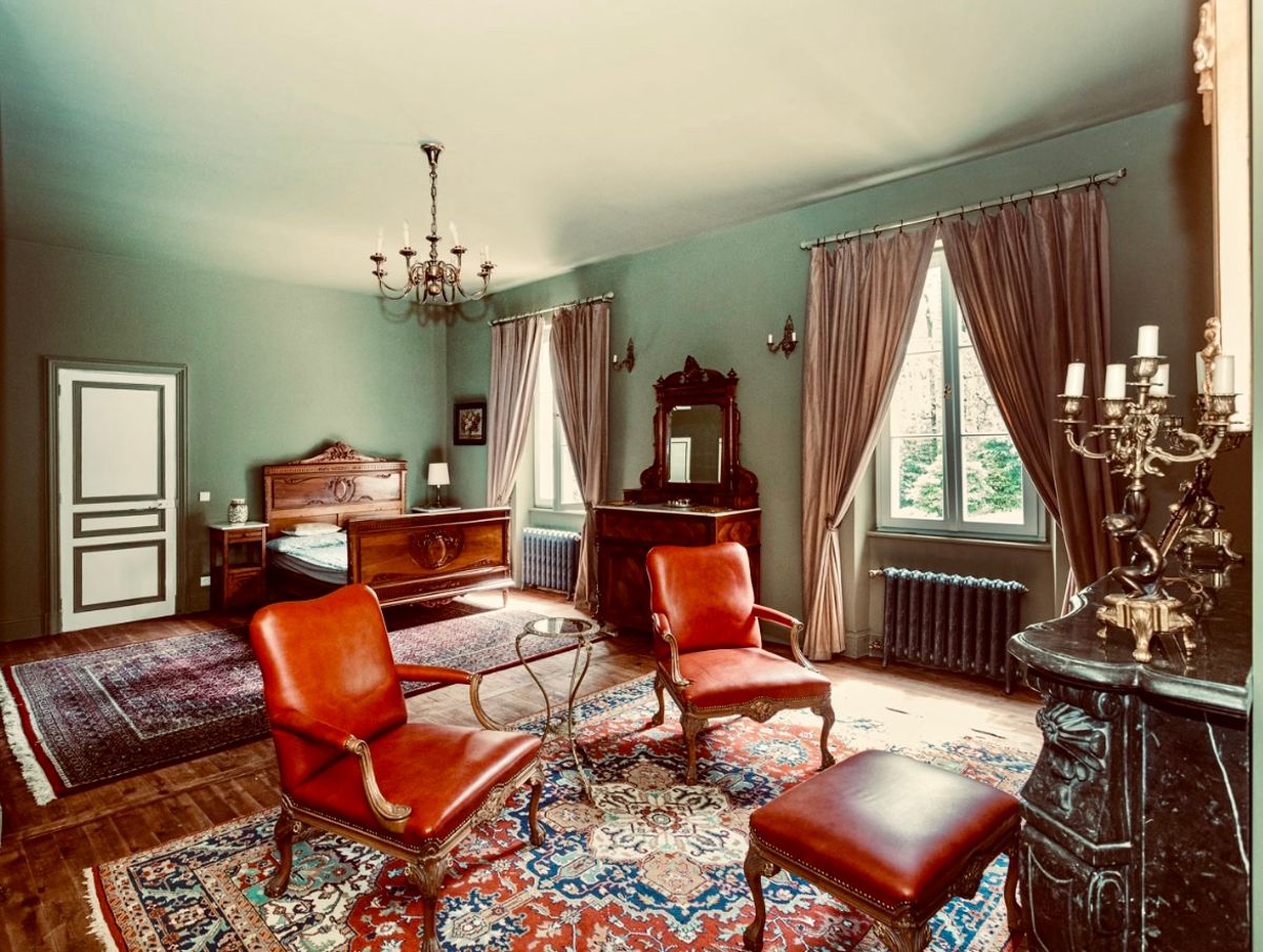 A bedroom with leather armchairs and a footstool, a carved bed and candelabra on the mantelpiece