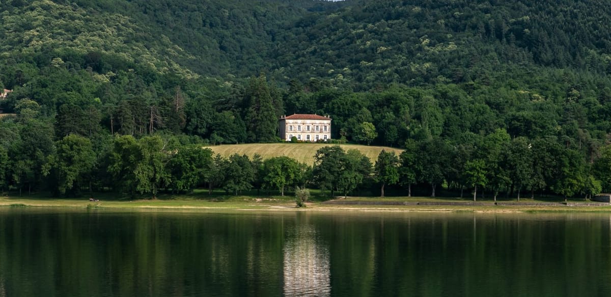 The château seen across the lake, in a clearing on the wooded hillside