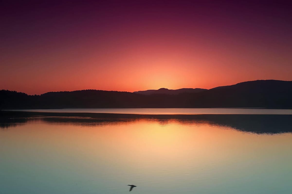 The sun low behind the hills, the sky reflected in a still lake