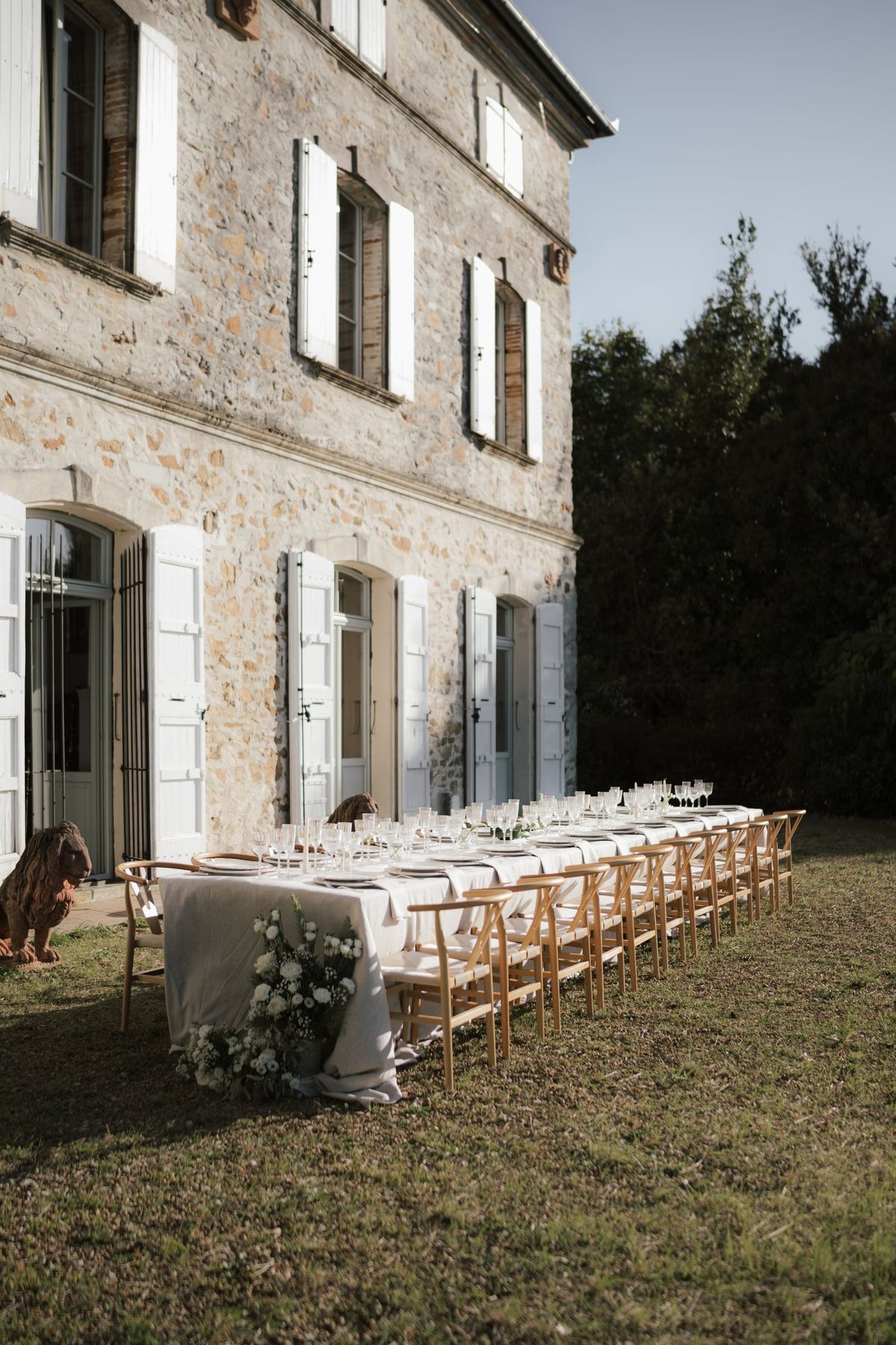 A long dinner table with wooden chairs set on the lawn alongside the château