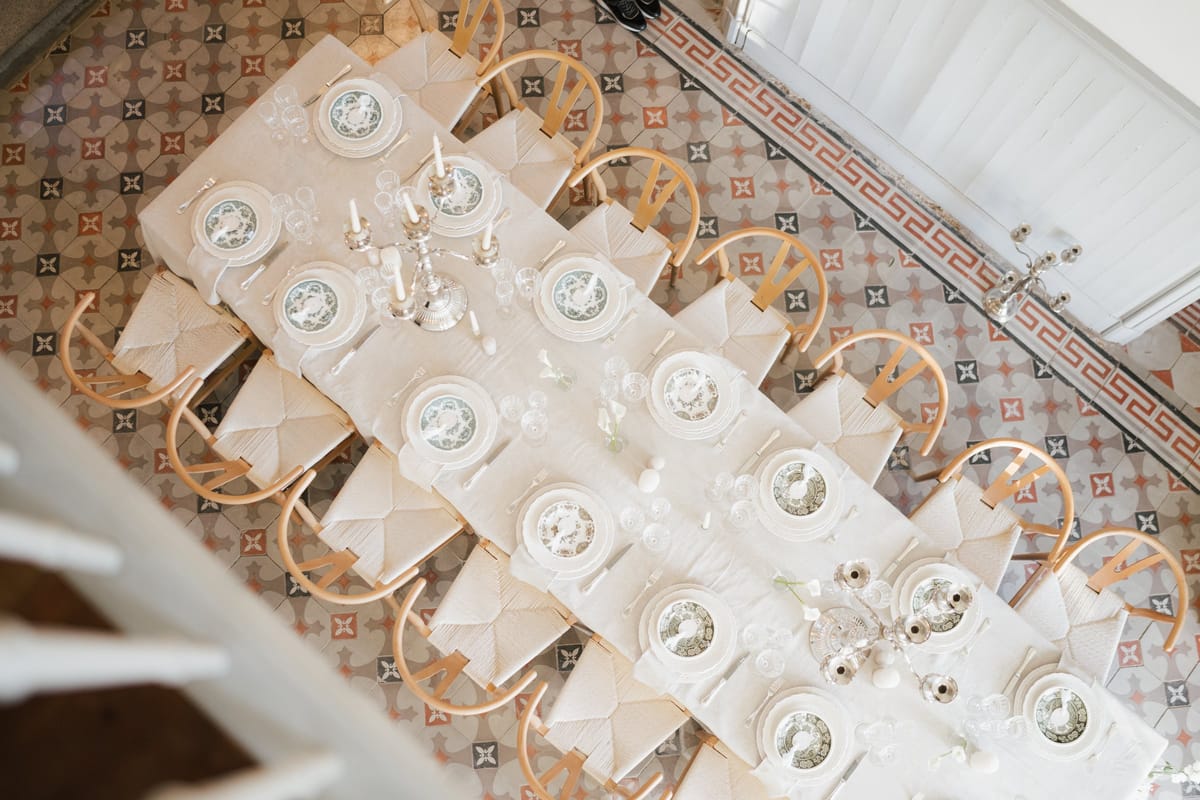 Overhead view of a long table laid with patterned plates, glassware and silver candelabra on a patterned tiled floor