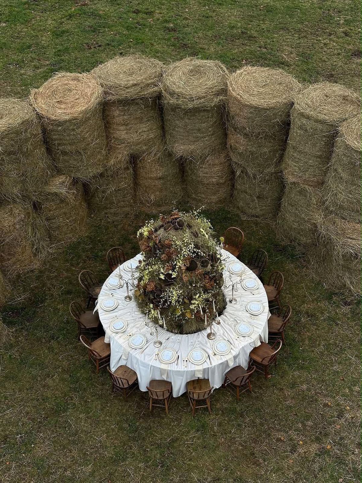 Overhead view of a round table with a tall dried-flower centrepiece, backed by a curved wall of round hay bales