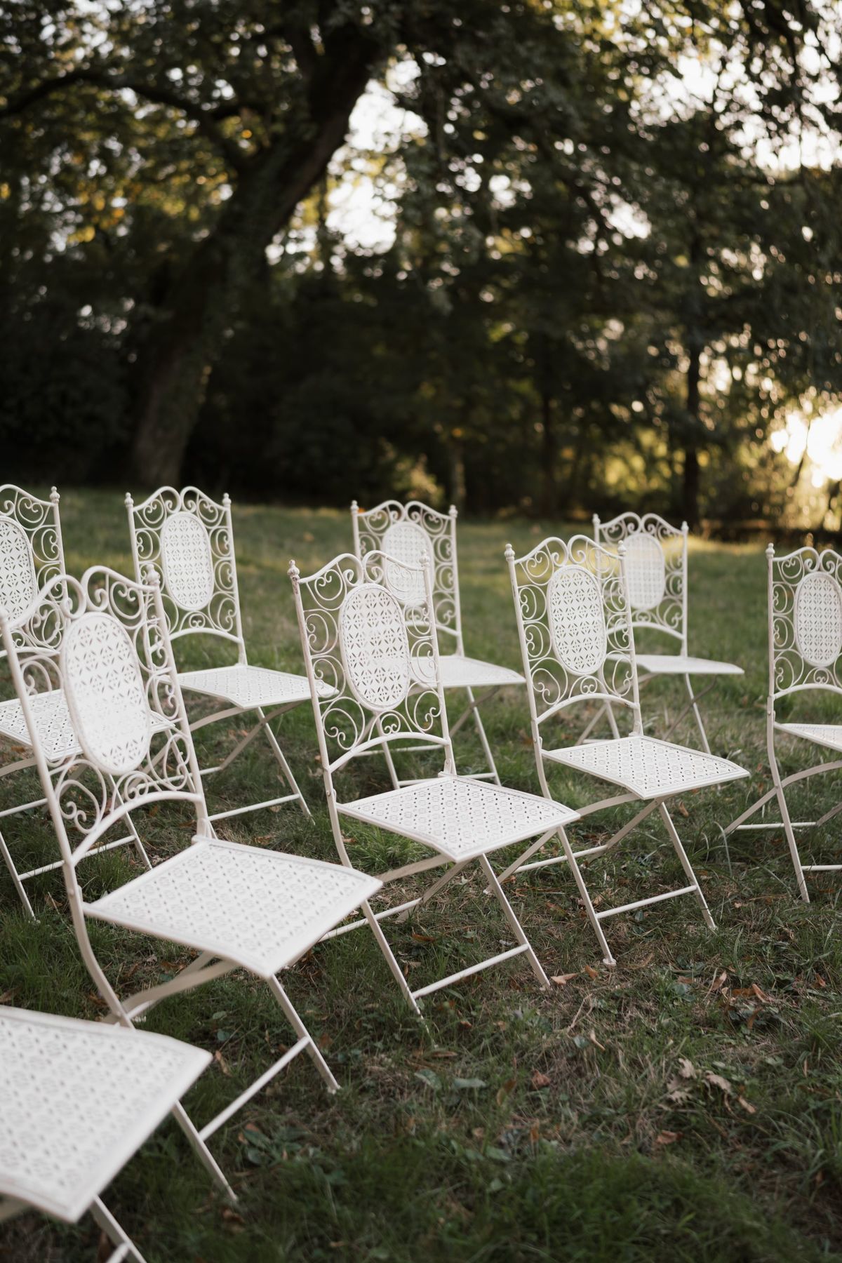 White wrought-iron chairs set on the lawn beneath the trees