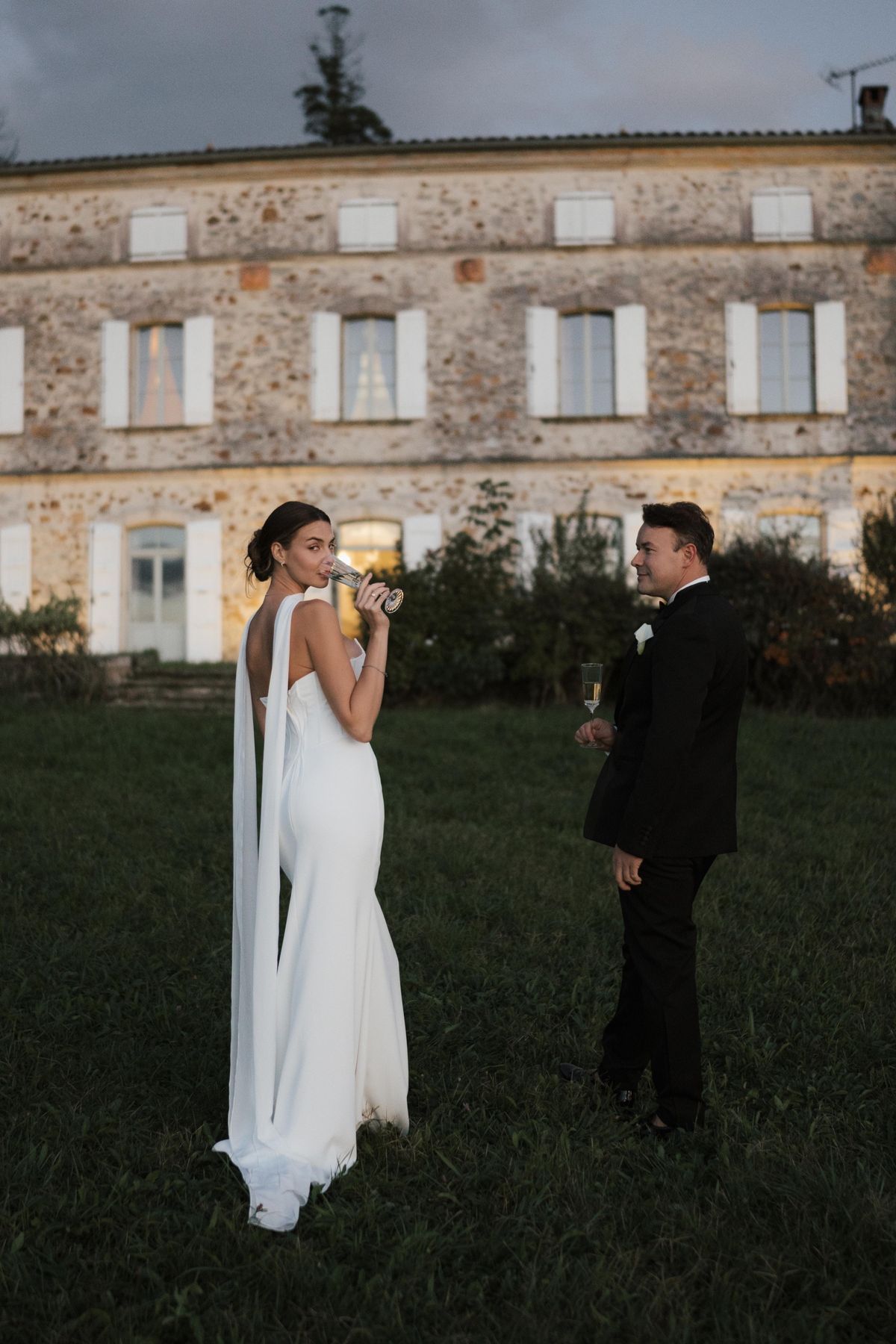 A couple sharing a champagne toast on the lawn in front of the château at dusk.