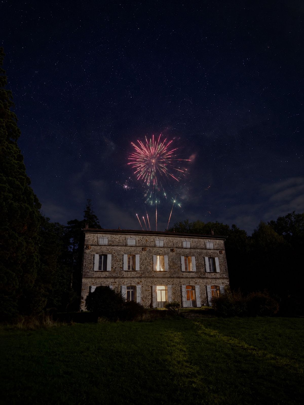 Fireworks over the illuminated stone facade of Château de L'Encastre at night.