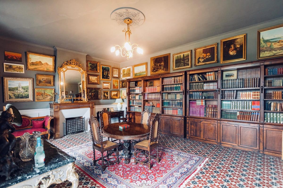 The château's library, with floor-to-ceiling bookshelves, framed paintings and a marble fireplace.