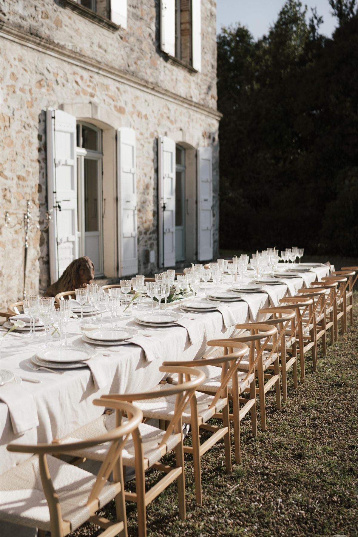 A long dining table set along the château's stone facade beneath the shuttered windows.