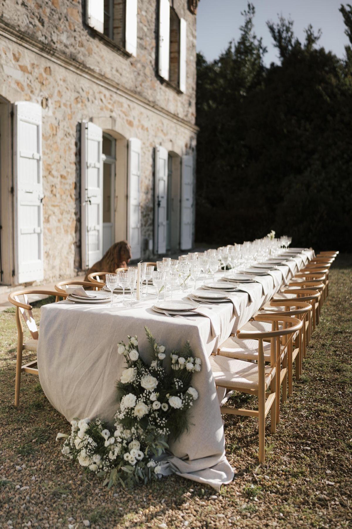 A long outdoor dining table with a trailing white floral runner, set before the château facade.