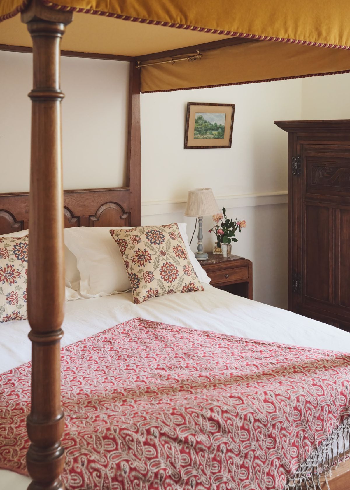 Four-poster bed with a mustard canopy, patterned cushions and a red paisley throw