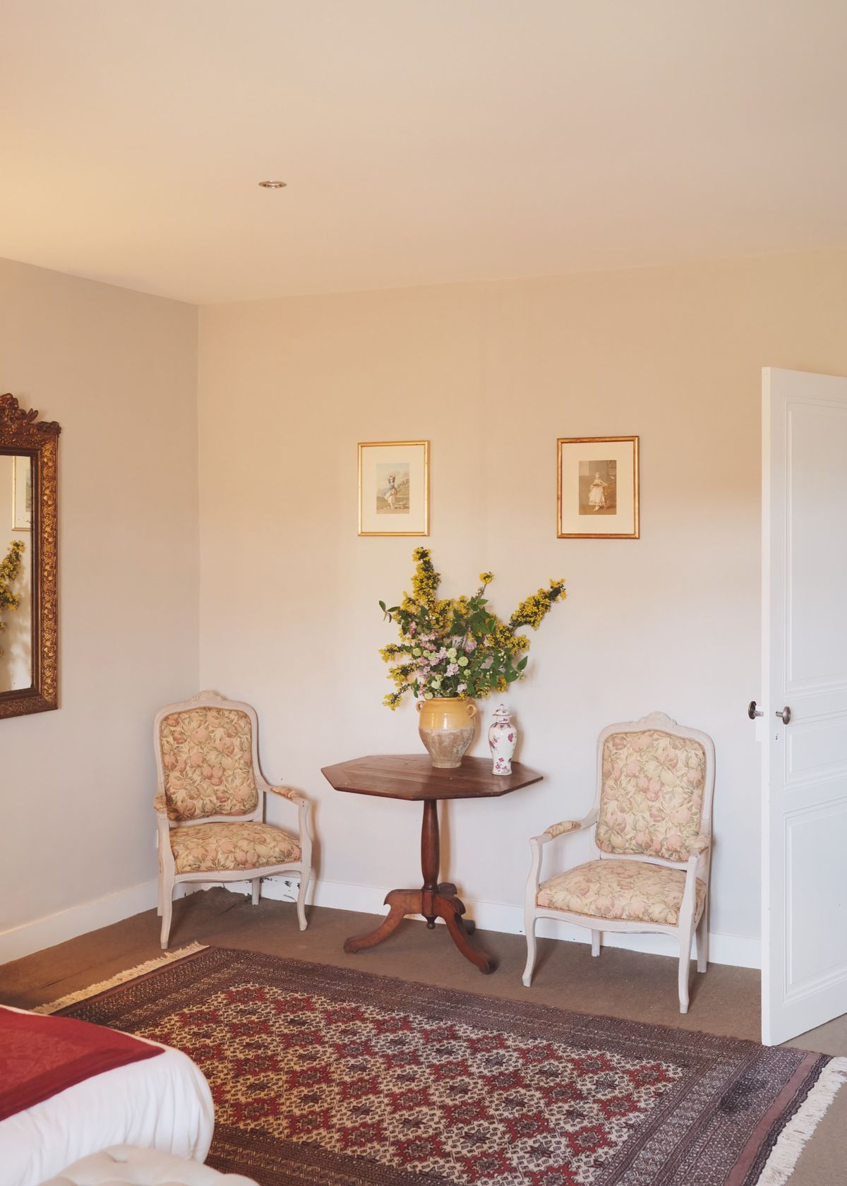 Corner of a bedroom with two upholstered armchairs either side of a small table with yellow flowers