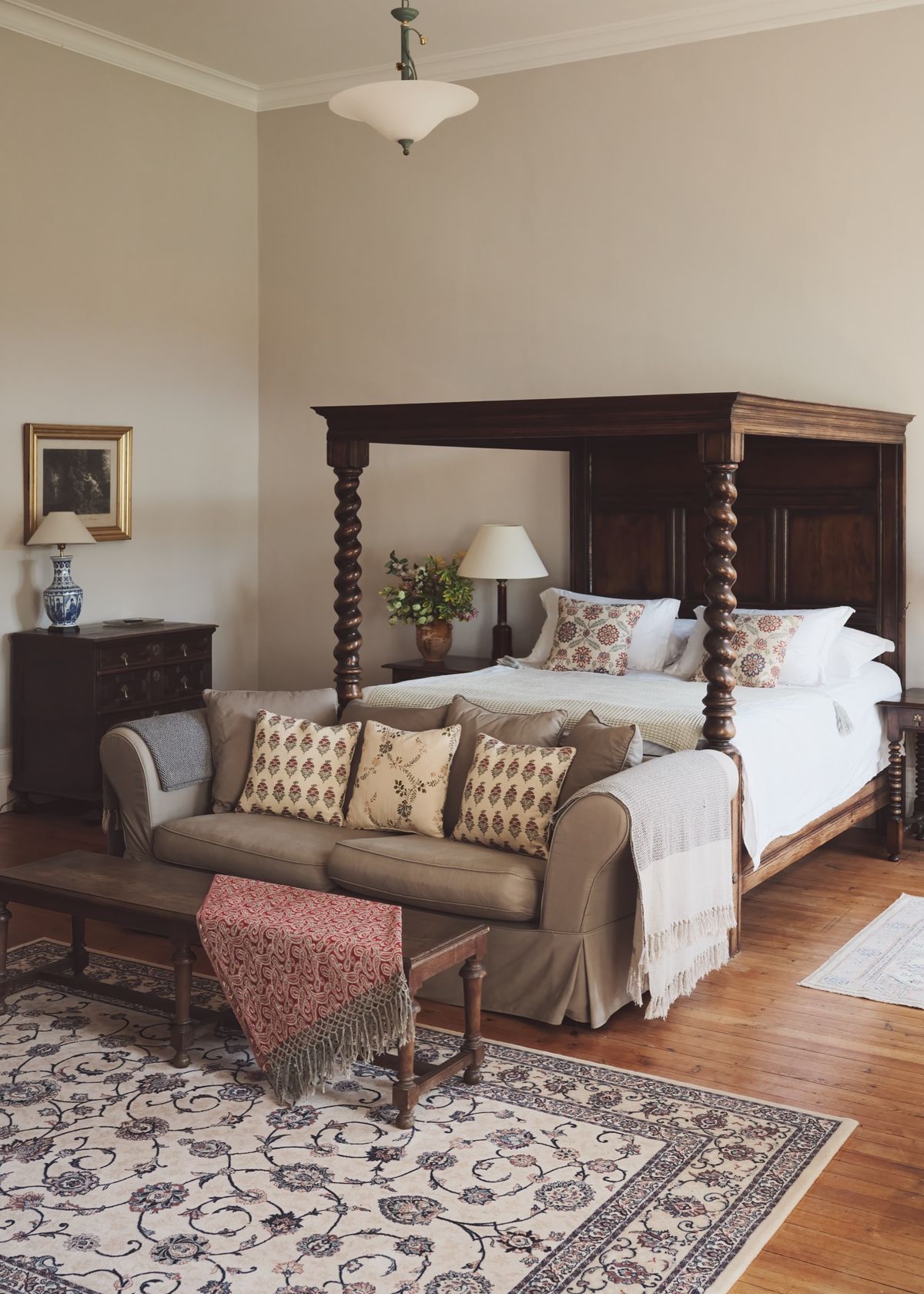 Bedroom with a barley-twist four-poster bed and a sofa piled with cushions on a patterned rug