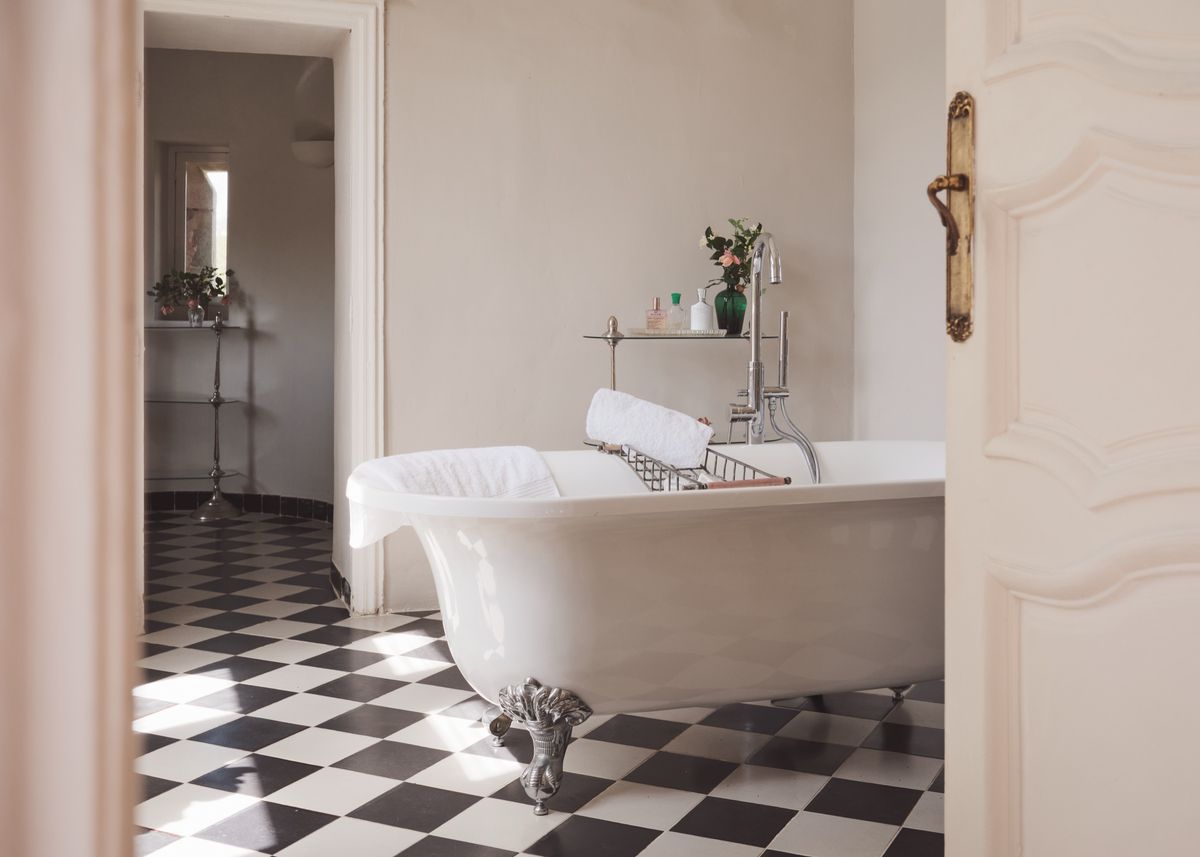 Claw-foot roll-top bath on black and white chequered tiles, seen through a panelled door
