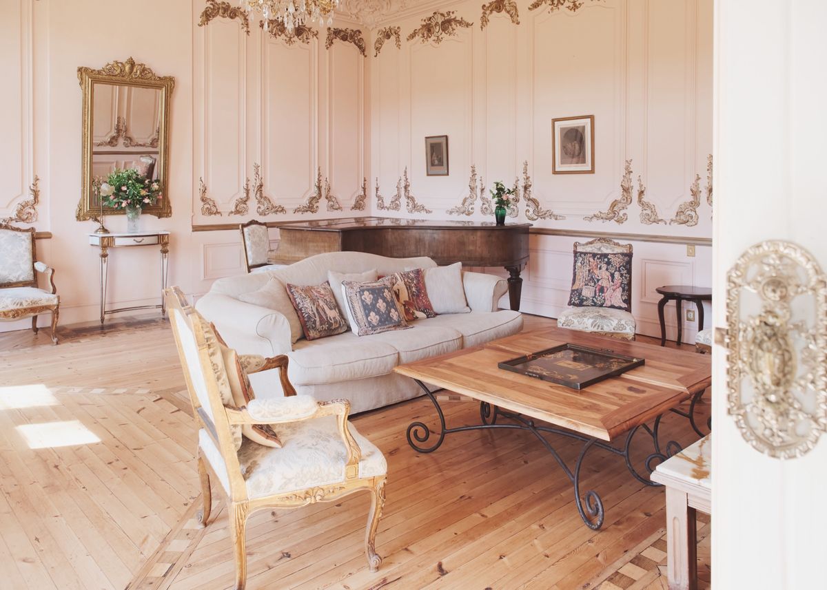 Drawing room with gilded wall mouldings, a cream sofa, carved armchairs and a low wood and iron table