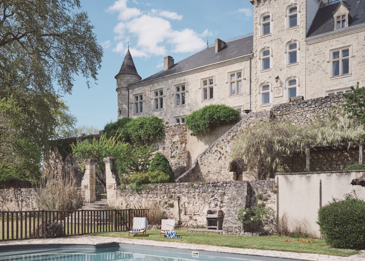 Swimming pool below the château's stone terraces, with a corner tower and tall windows under a blue sky