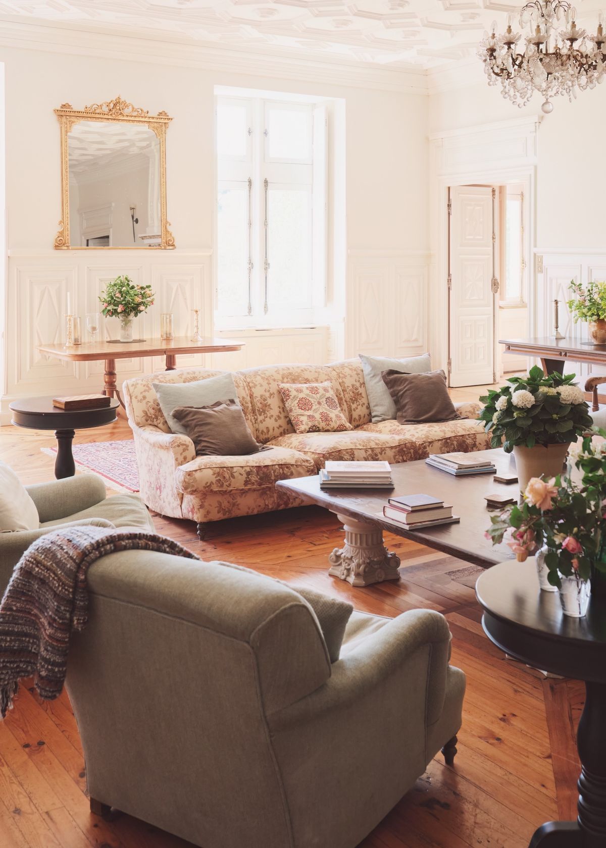 Bright sitting room with a floral sofa, a crystal chandelier, a gilded mirror and wooden floors