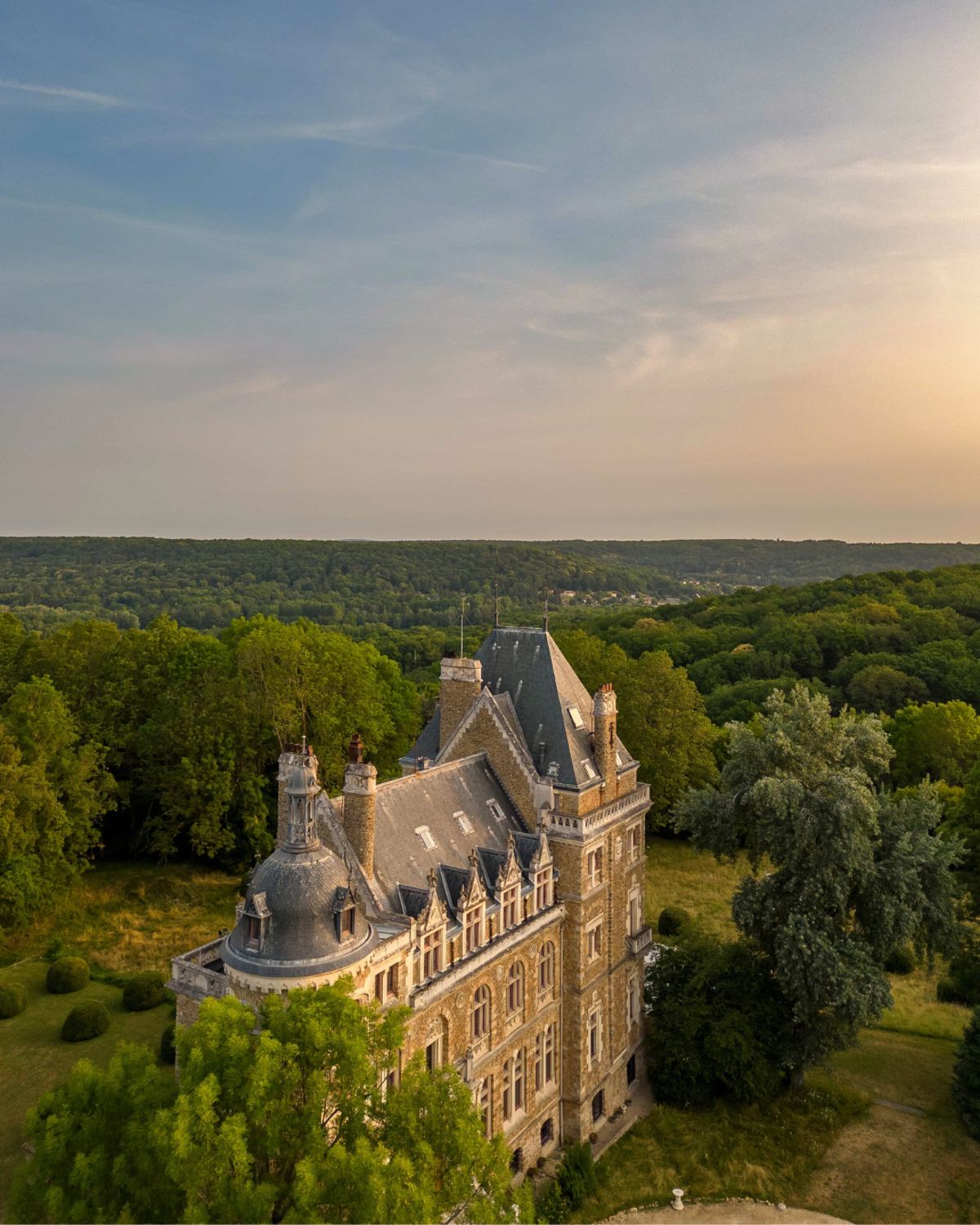 Aerial view of Château de Méridon at golden hour, surrounded by forest with sunset sky