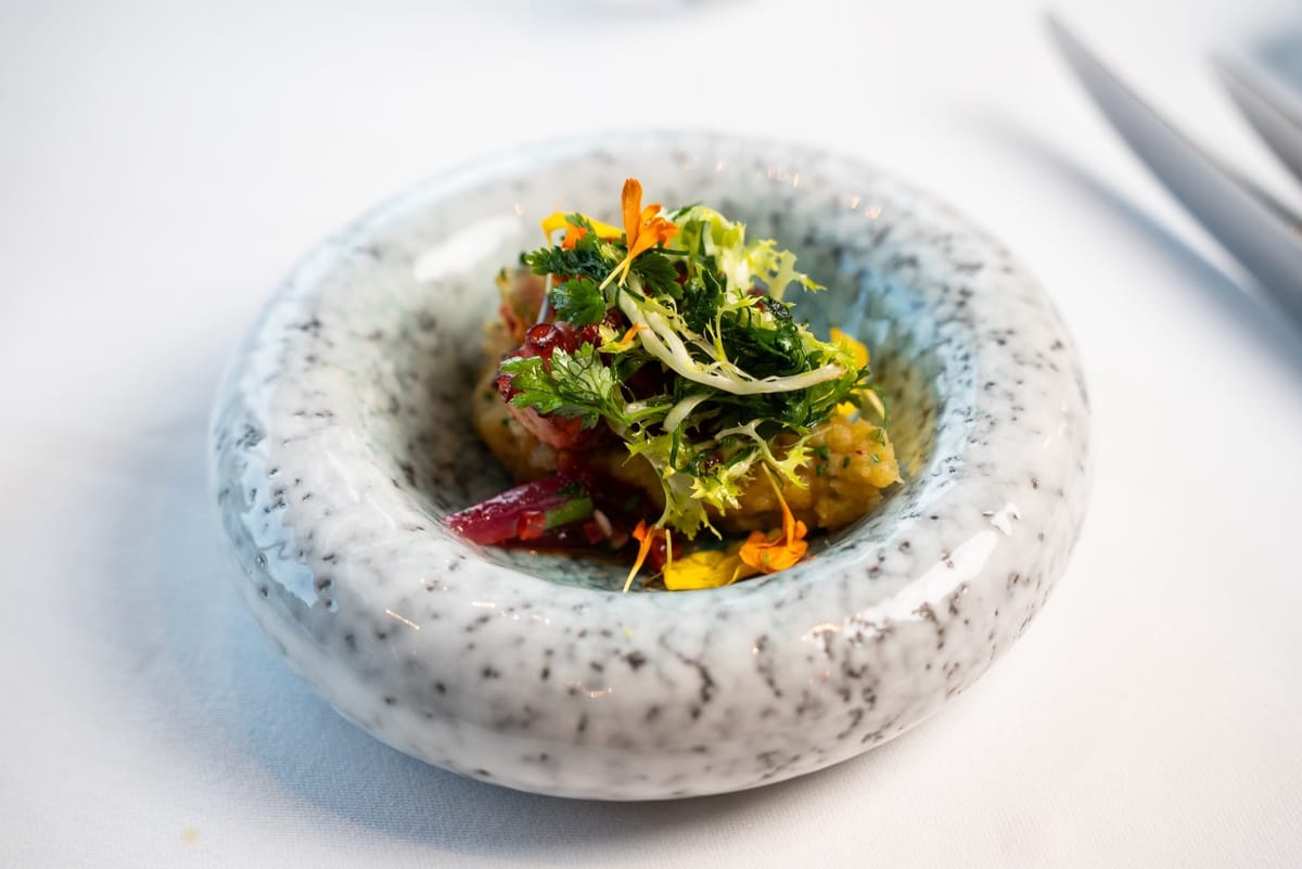 Octopus on crushed potato with pickled red onion, topped with frisée, herbs and nasturtium petals, in a speckled bowl