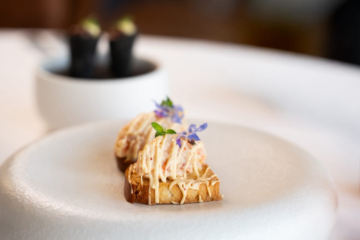 Crab-topped toasts garnished with borage flowers on a white plate