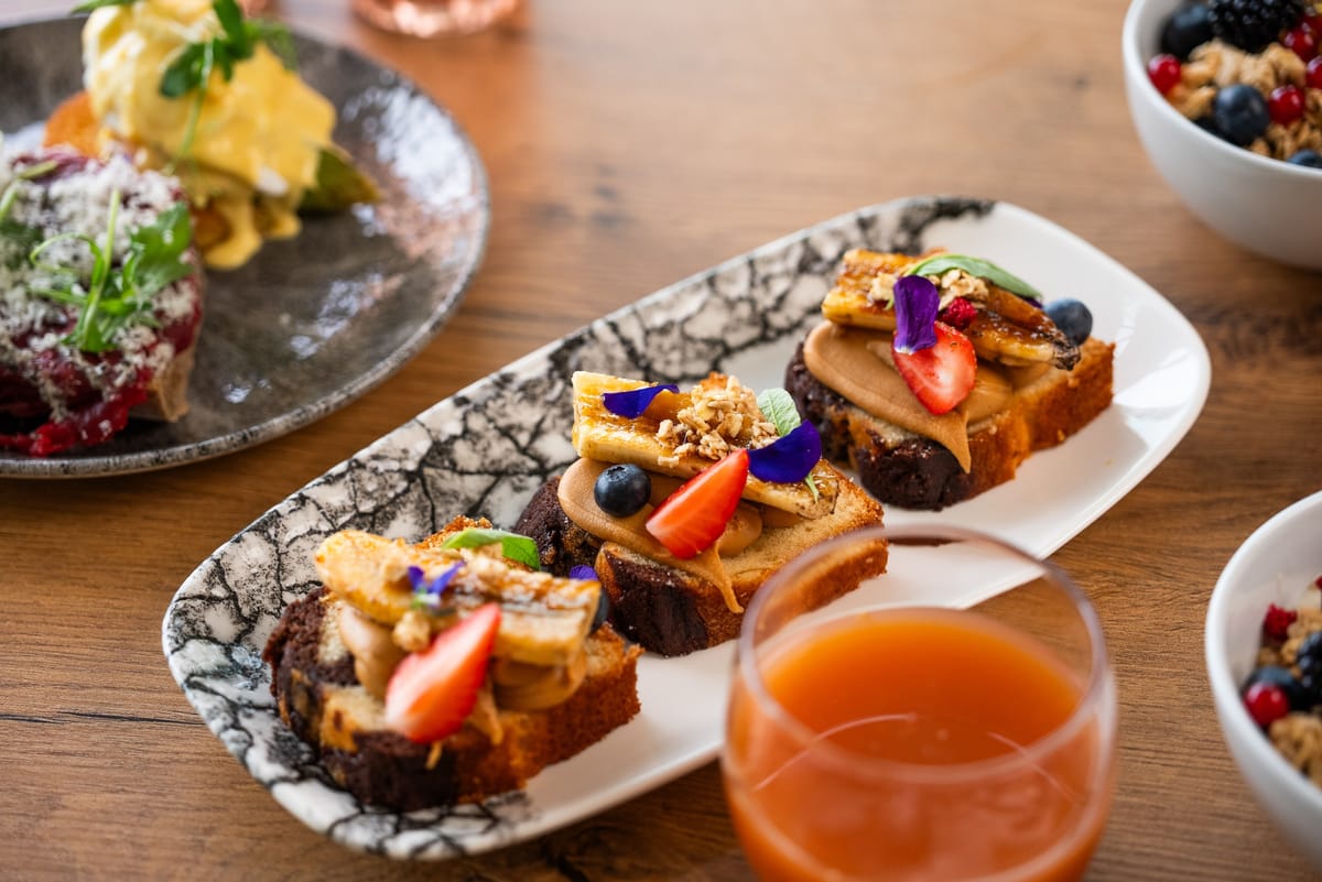 Slices of marble cake topped with caramelised banana, strawberries and edible flowers on a platter with a glass of juice