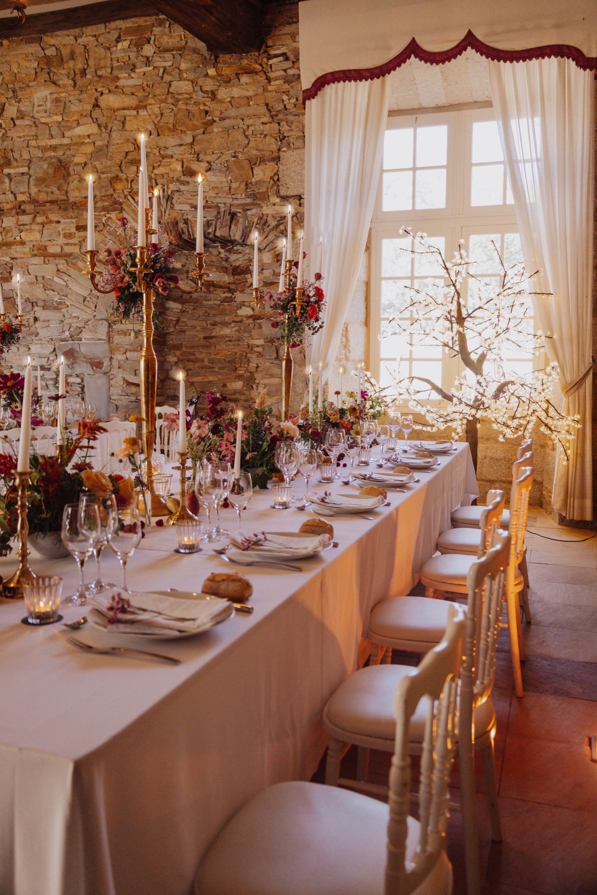 Long banquet table in the stone-walled hall at Chateau du Pordor, set with candelabra and autumn flowers