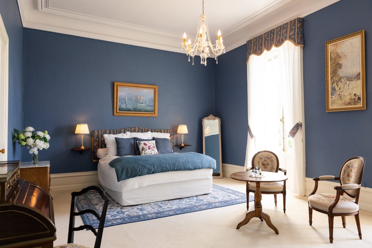 Bridal suite bedroom at Chateau du Pordor with a chandelier, teal bedcover and a seating area by the window