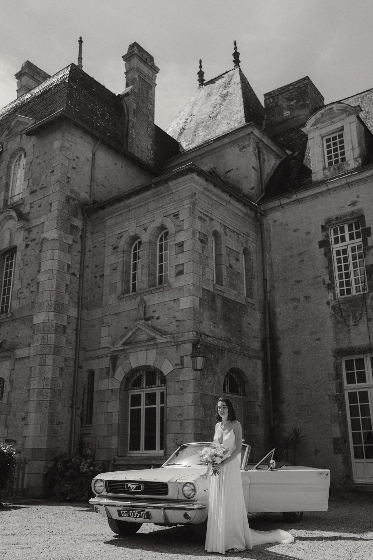 A bride beside a classic convertible in front of the facade at Chateau du Pordor