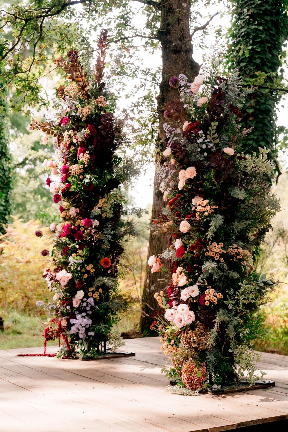 Two tall floral columns flanking the wooden ceremony platform in the grounds at Chateau du Pordor