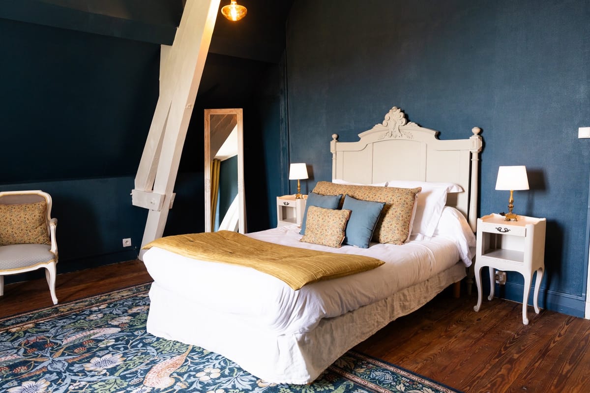 The Comte et Comtesse room at Chateau du Pordor, a beamed bedroom with a carved headboard and dark teal walls