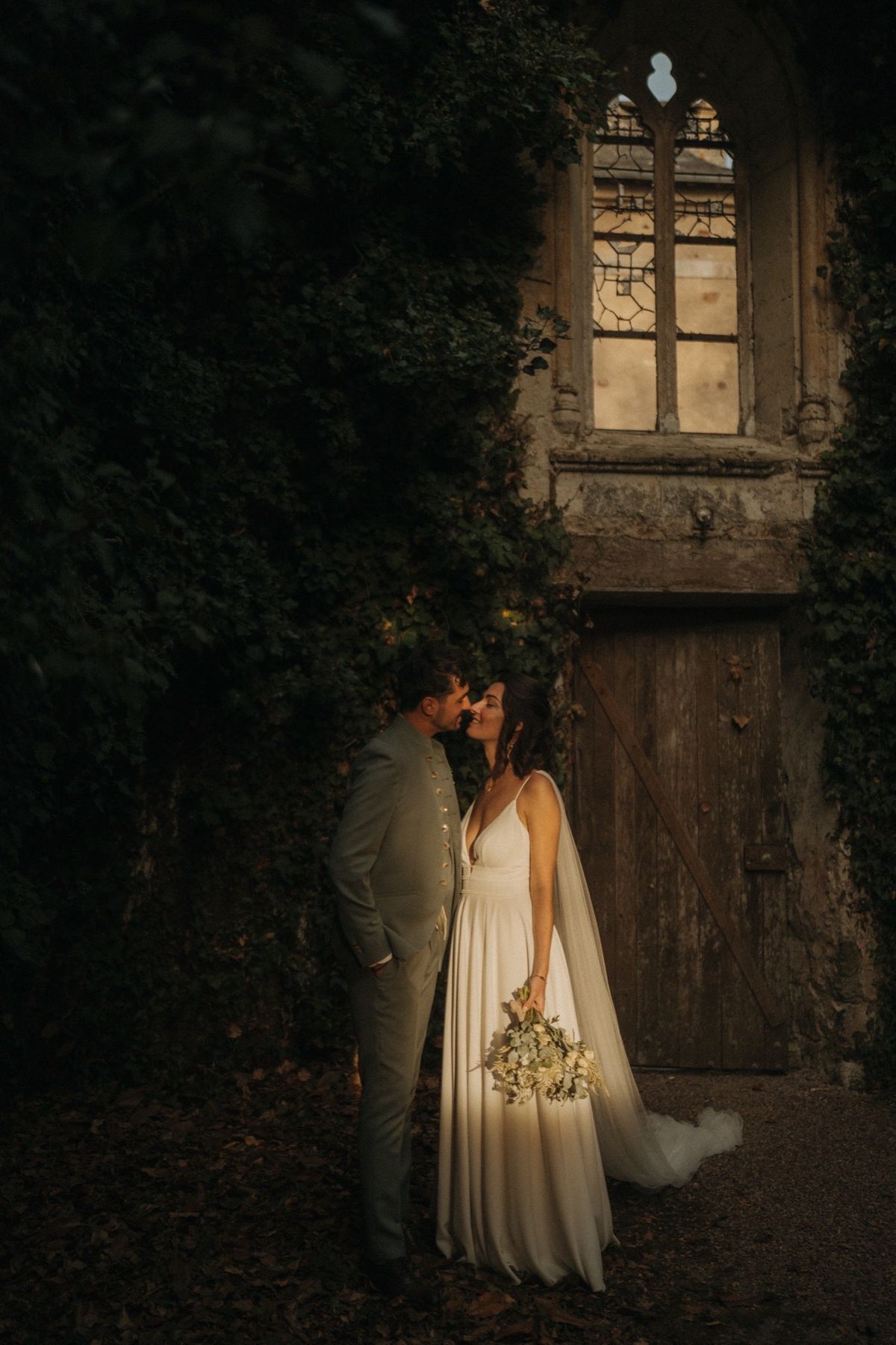 A couple beside the ivy-covered stone wall and old wooden door at Chateau du Pordor at dusk