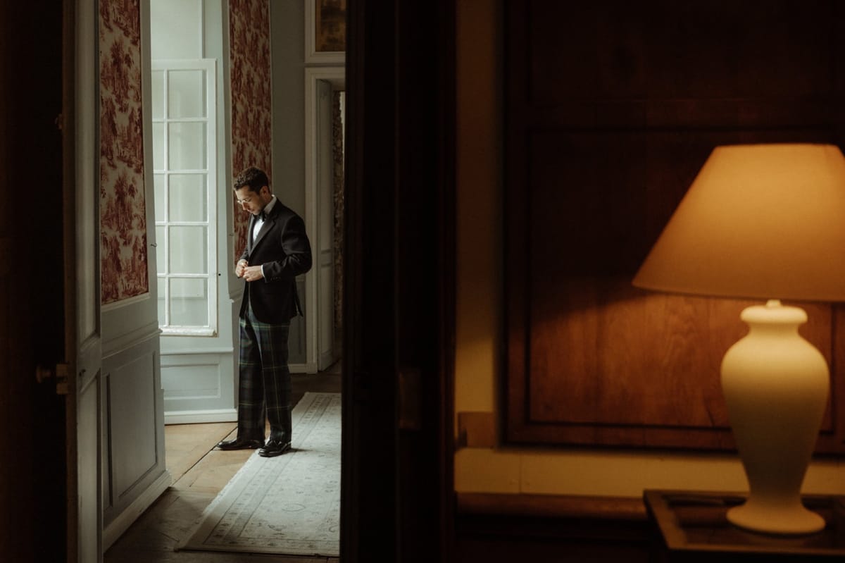 A groom dressing in a guest room at Chateau du Pordor, seen through the doorway