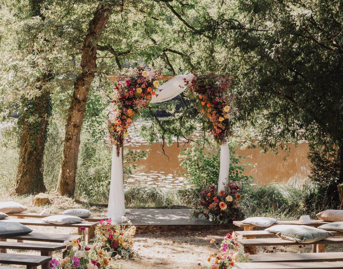 Outdoor ceremony arch at Chateau du Pordor dressed with autumn flowers, with floor cushions and benches under the trees