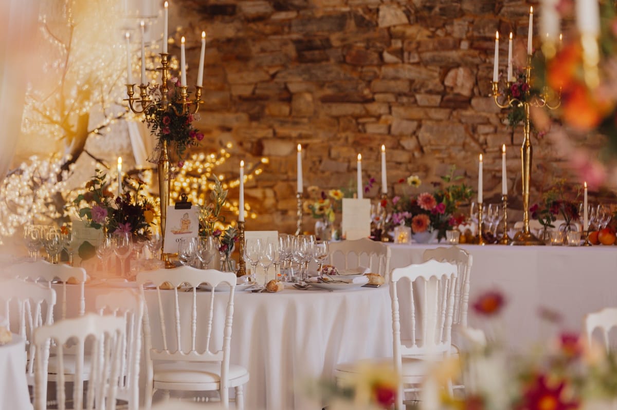 Round tables set for dinner in the stone-walled reception hall at Chateau du Pordor, lit by candelabra