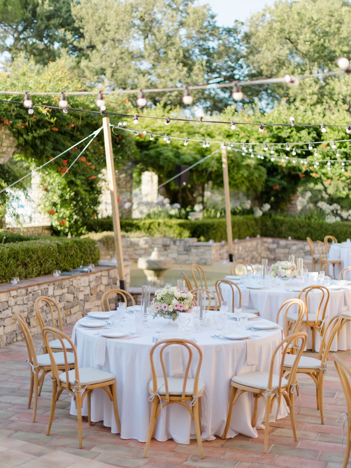 Round tables set for a wedding dinner under festoon lights at Chateau les Crostes