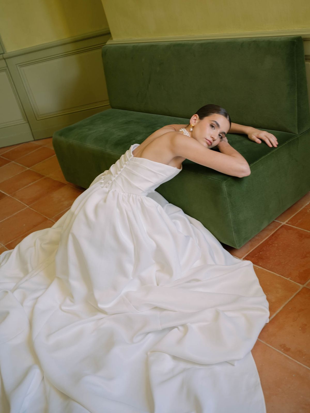 Bride reclining on an emerald-green velvet sofa against olive walls at Château de l'Hospital