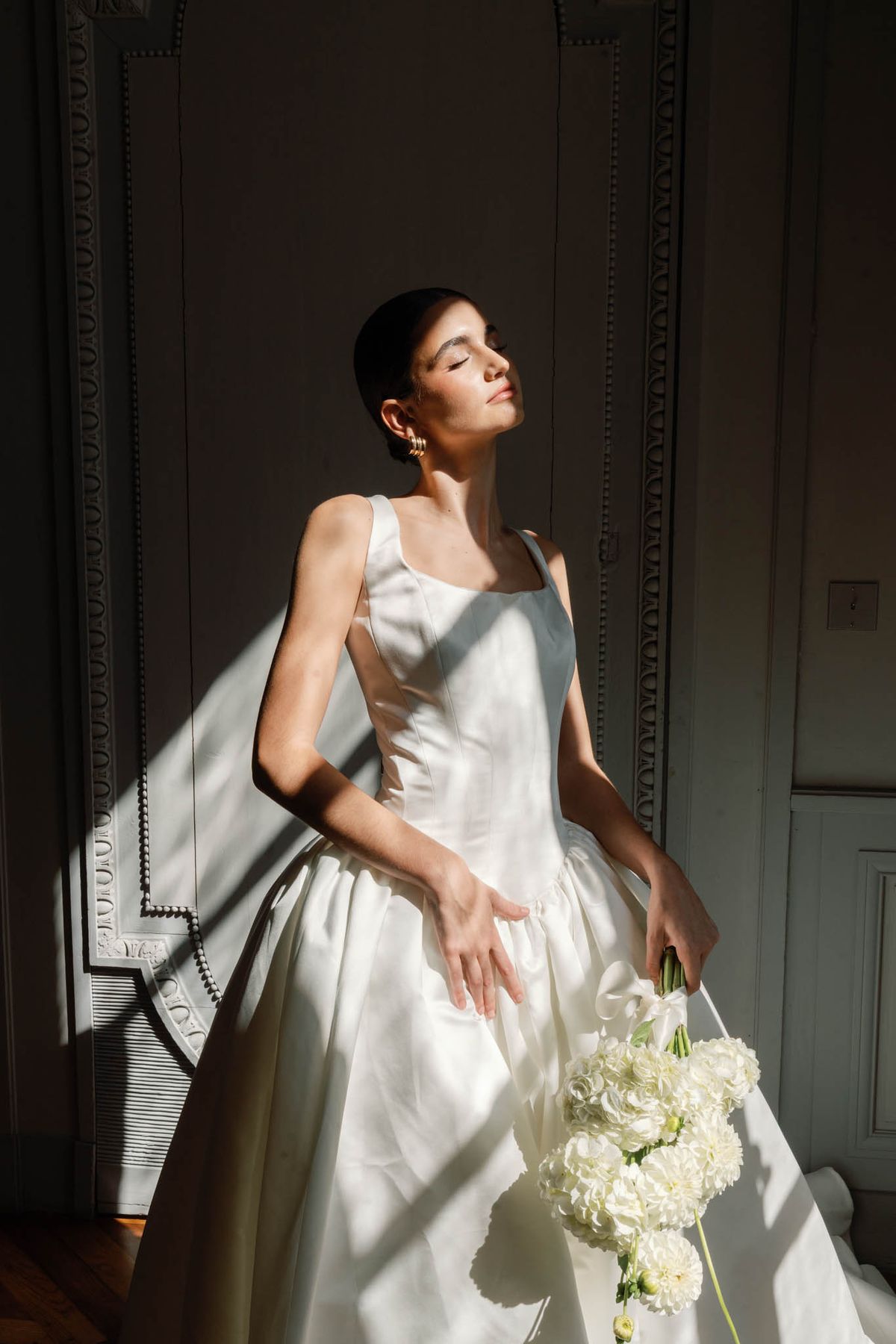 Serene bride holding white dahlia bouquet in a sunlit panelled room at Château de l'Hospital