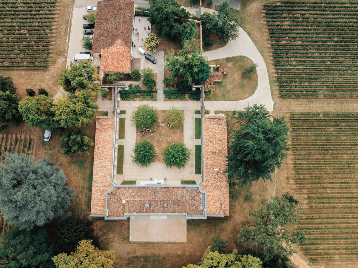 Wide aerial view of Chateau de l'Hospital estate, vineyards and the village of Portets beyond