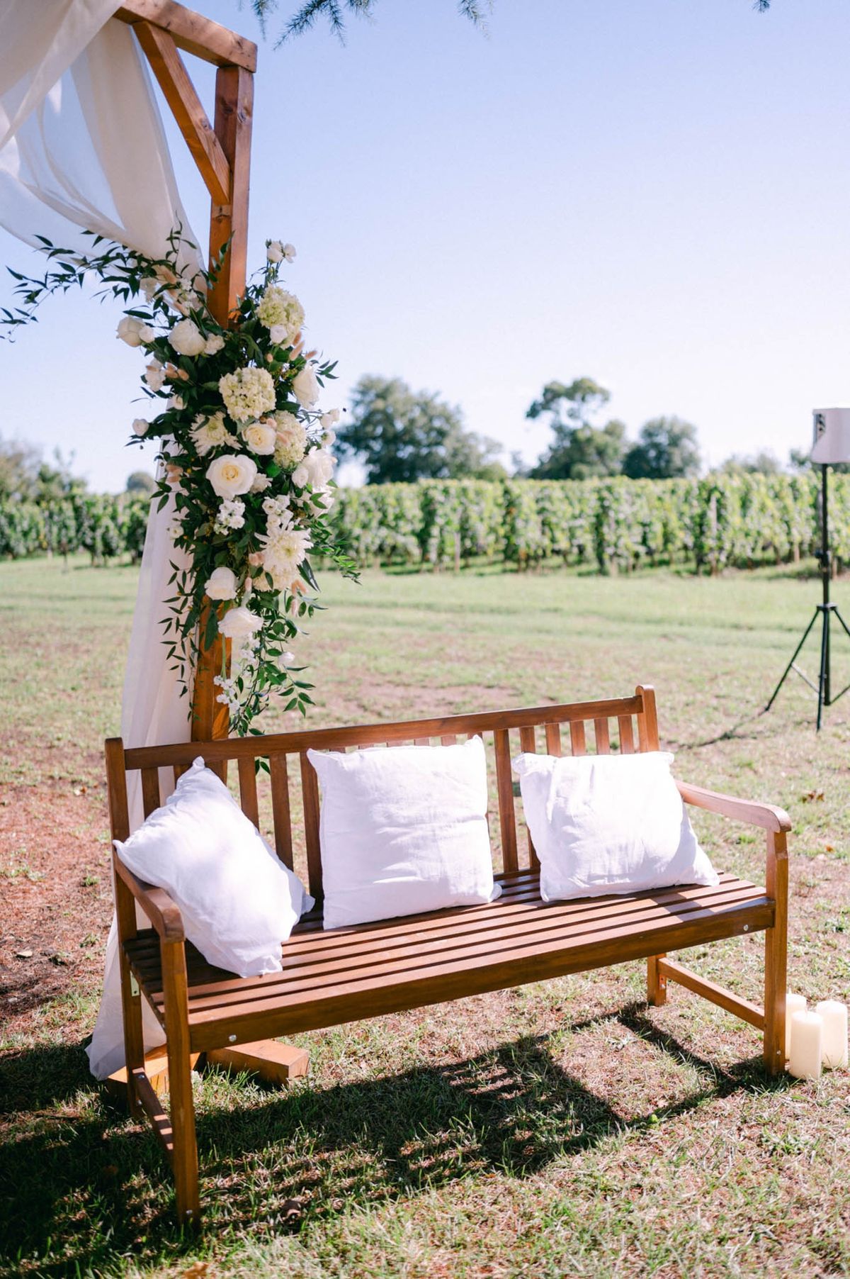 Wooden bench with a pampas and fresh-bloom arch set on the lawn with the estate vineyard beyond