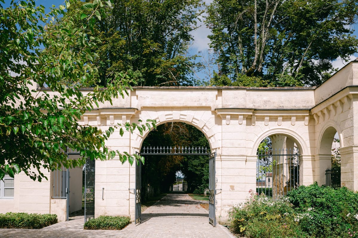 Stone gateway arch at the main entrance of Chateau de l'Hospital with wrought-iron gates