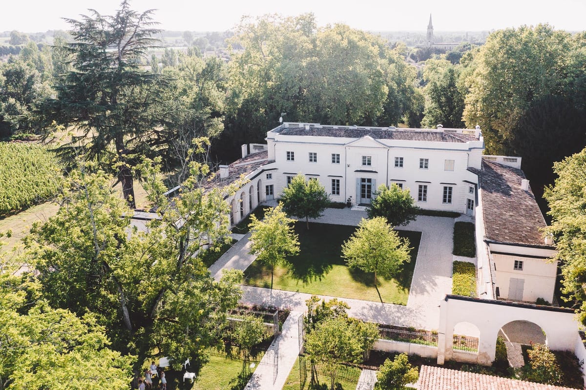 Aerial side view of Chateau de l'Hospital with lawns, trees and outbuildings