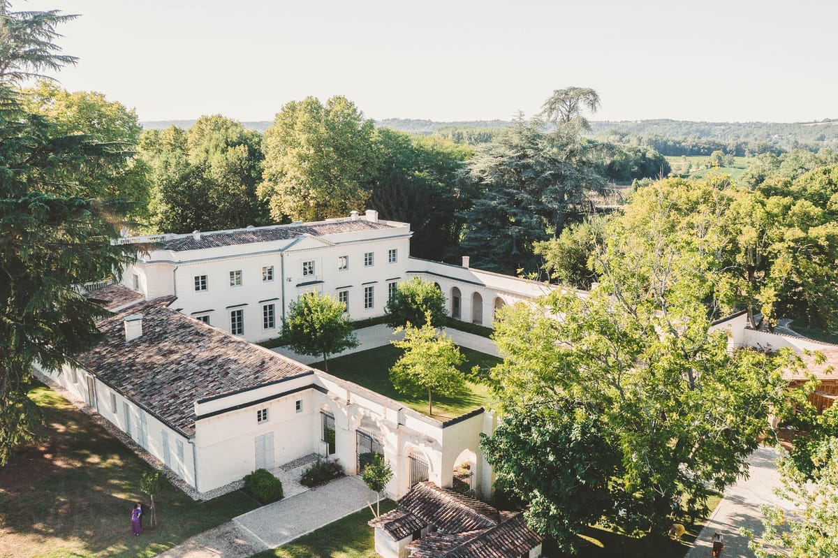 Aerial view of Chateau de l'Hospital estate with outbuildings and distant woodland