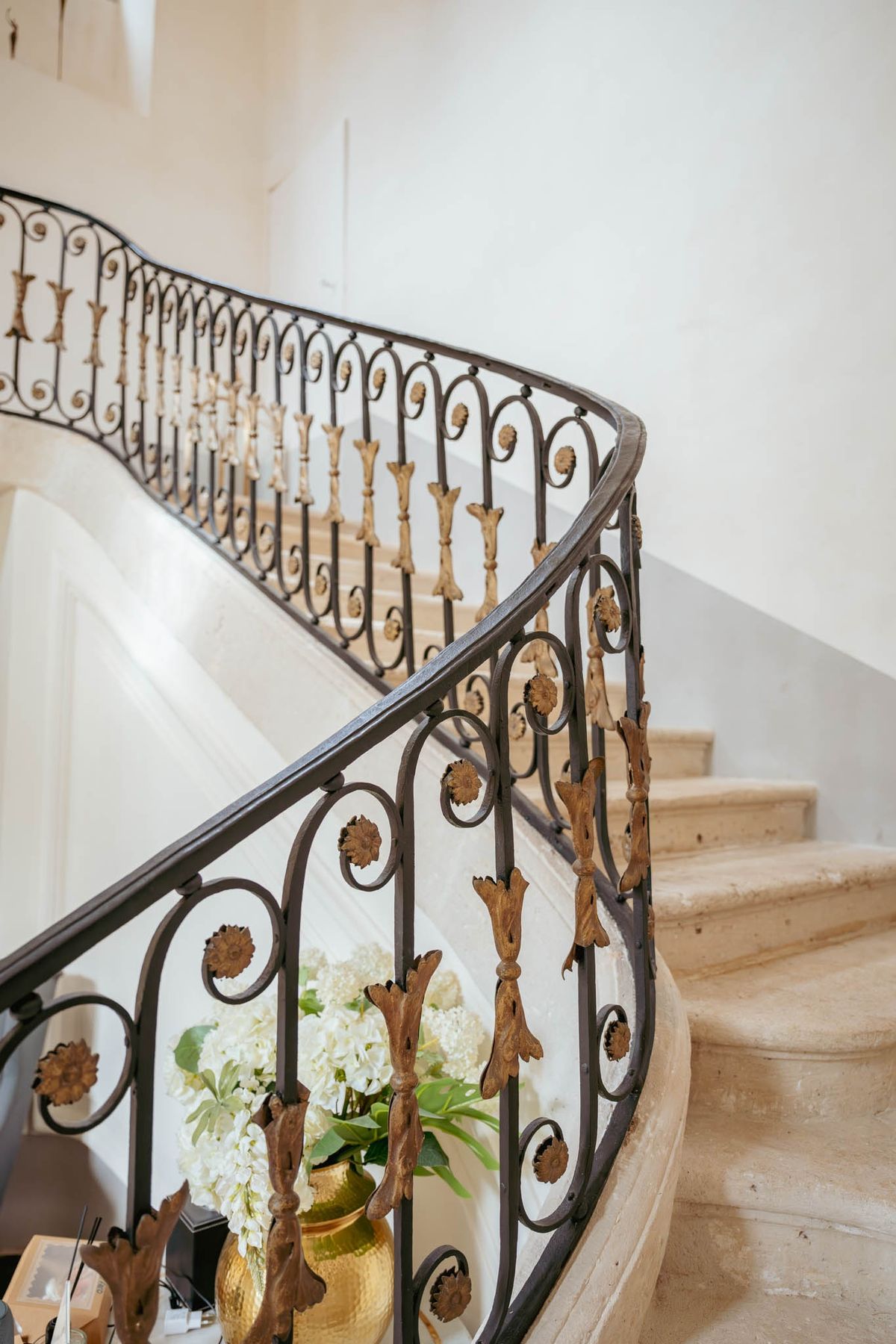Wrought-iron staircase with gold-leaf detailing and a hydrangea arrangement at its base, inside Chateau de l'Hospital