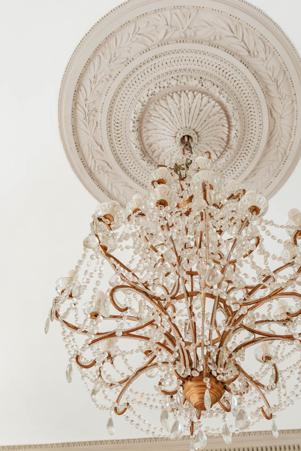 Close-up of a crystal chandelier hanging from an ornate plaster ceiling rosette at Chateau de l'Hospital