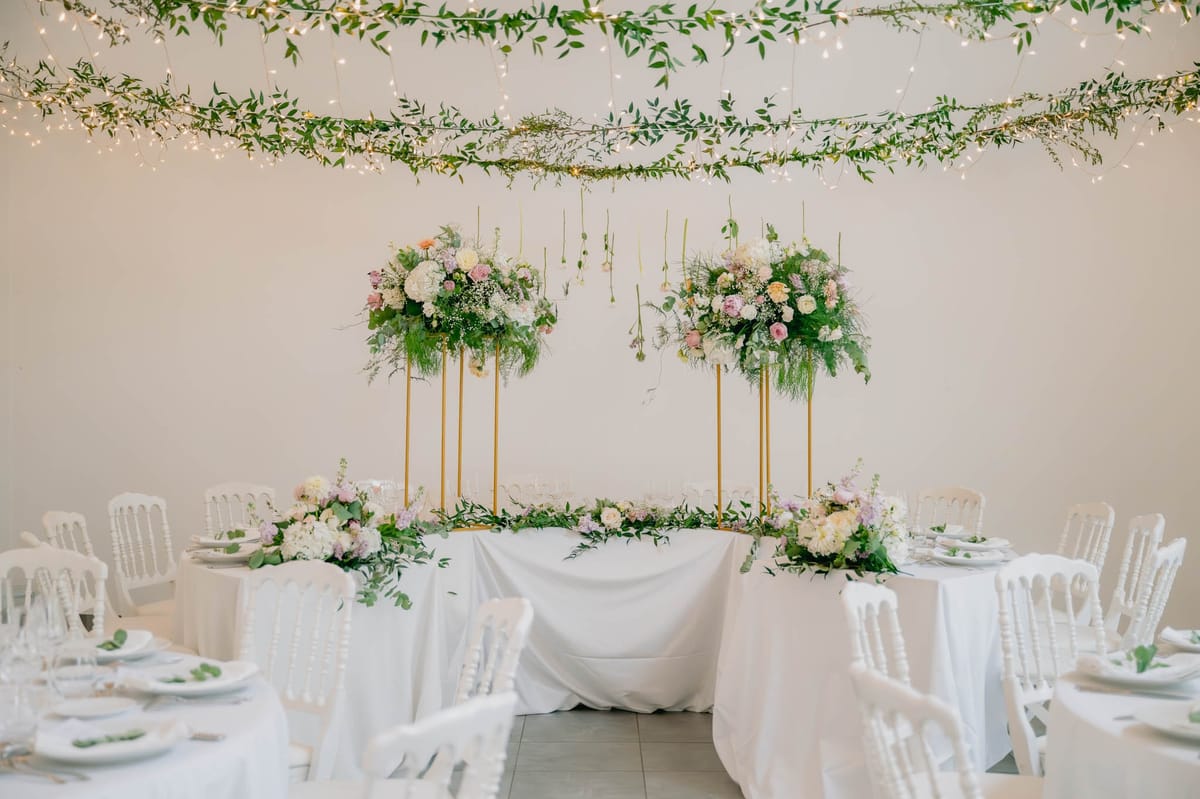Orangery Hall at Chateau de l'Hospital set with a fairy-light greenery canopy, tall floral centrepieces and long wooden tables