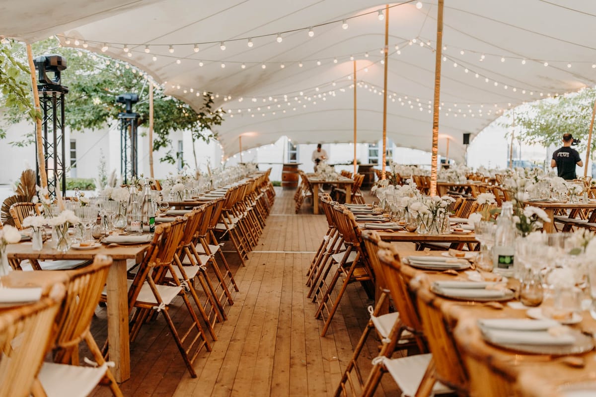 Stretch tent reception at Chateau de l'Hospital with long wooden tables, candles and festoon lighting