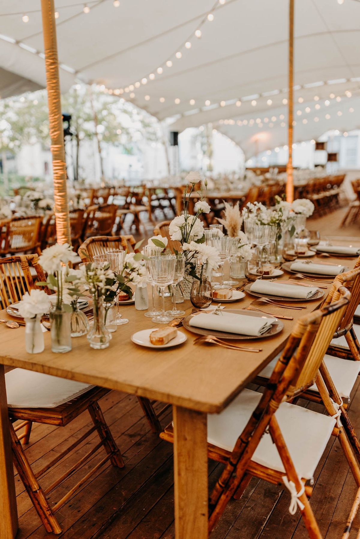 Stretch tent dining at Chateau de l'Hospital with wooden tables, floral runners and amber glassware