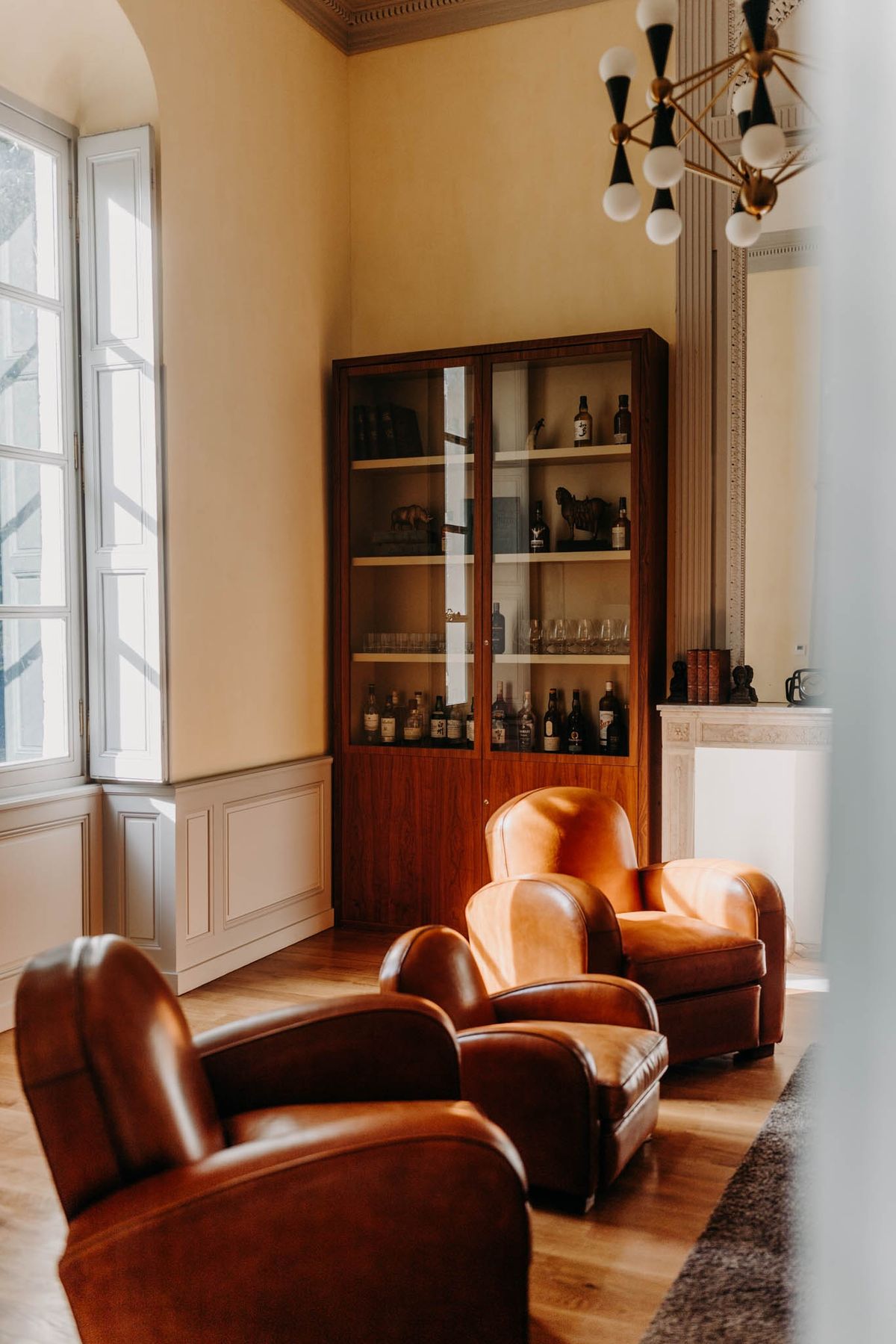 Cigar Room at Chateau de l'Hospital with brown leather club chairs, a vintage drinks cabinet and chandelier