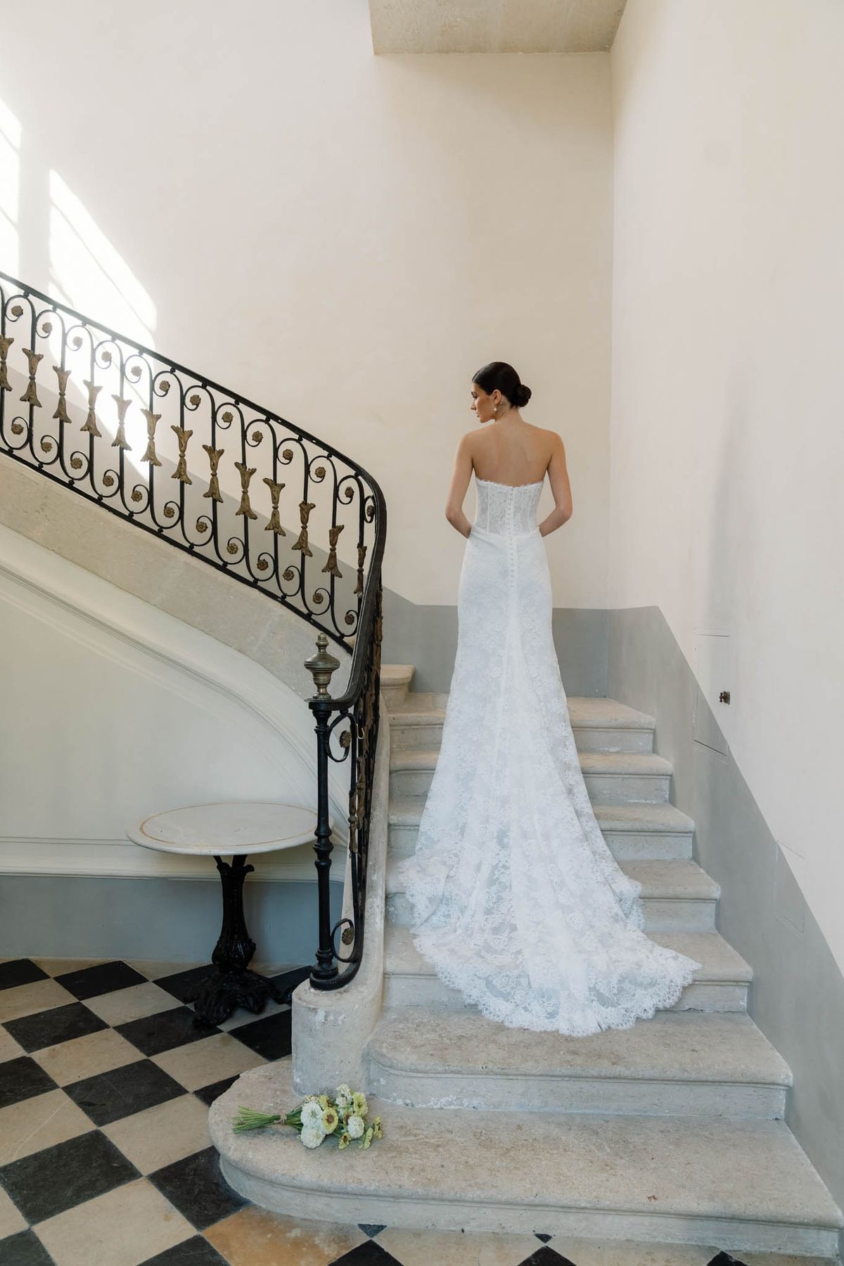 Bride standing on the chequerboard marble stair landing at Chateau de l'Hospital with the wrought-iron balustrade