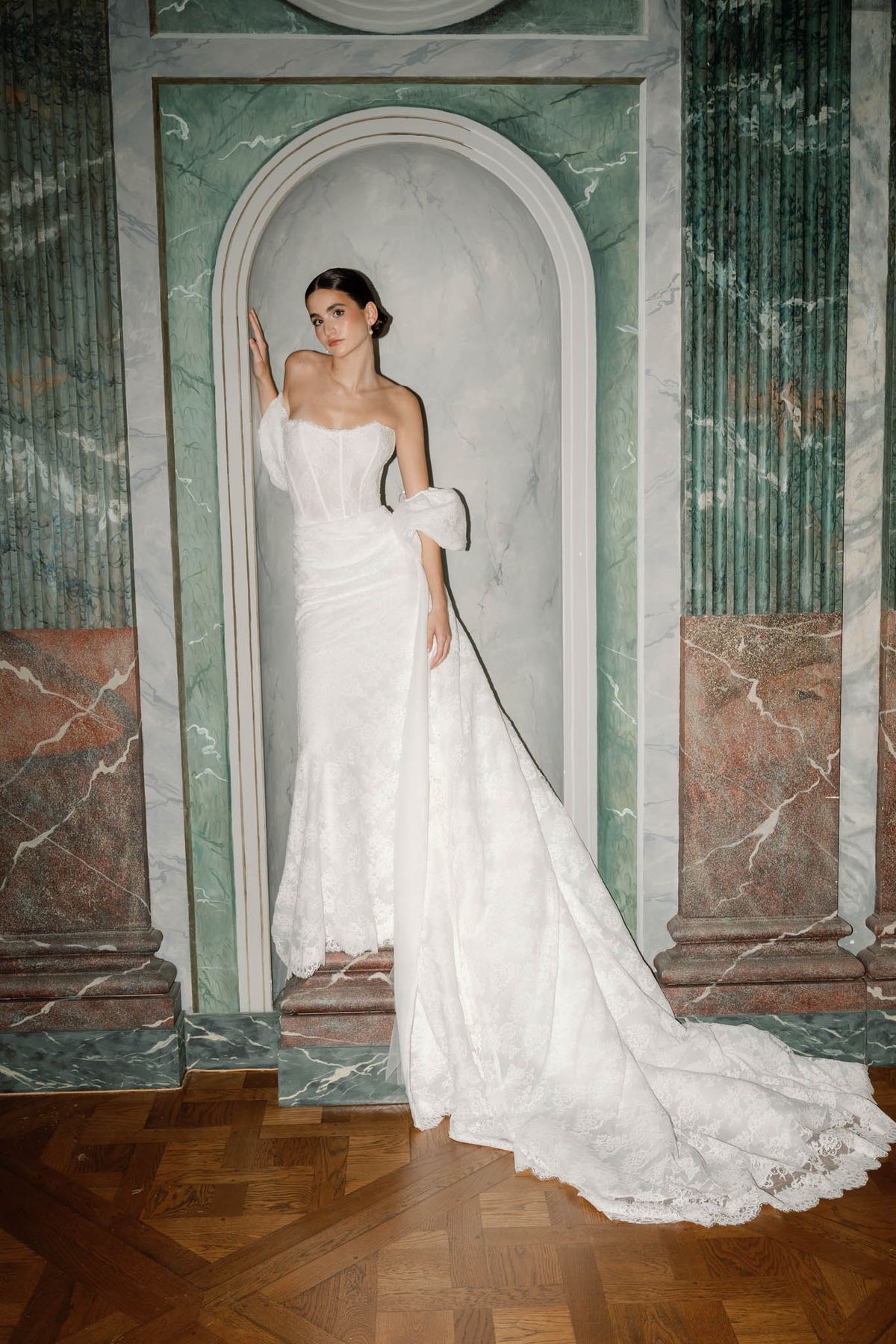 Bride in a white off-shoulder lace gown posed in a trompe-l'oeil marble alcove at Chateau de l'Hospital