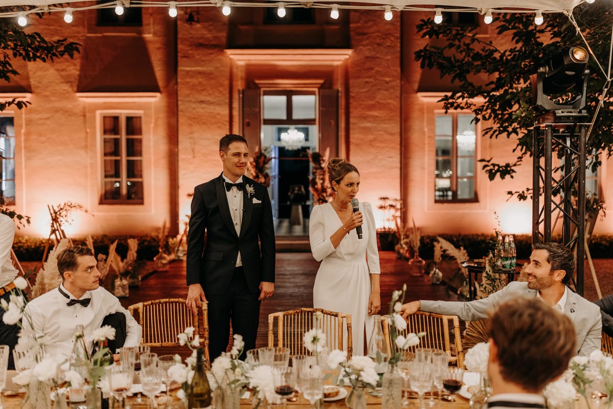 Château de l'Hospital's floodlit facade at night during the wedding reception, with festoon lighting under the marquee